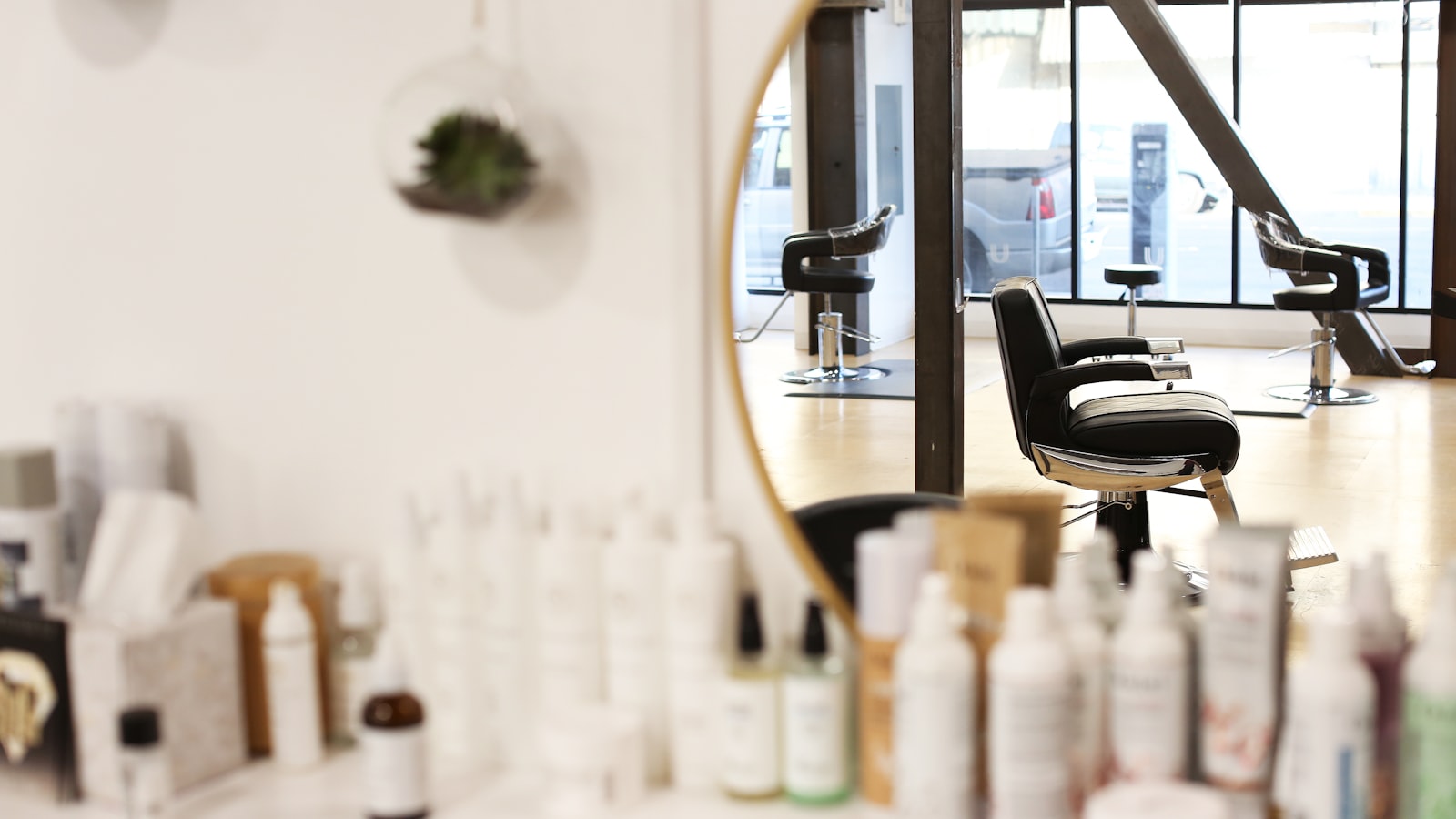 An empty salon chair reflected in a round mirror at a bright hair salon