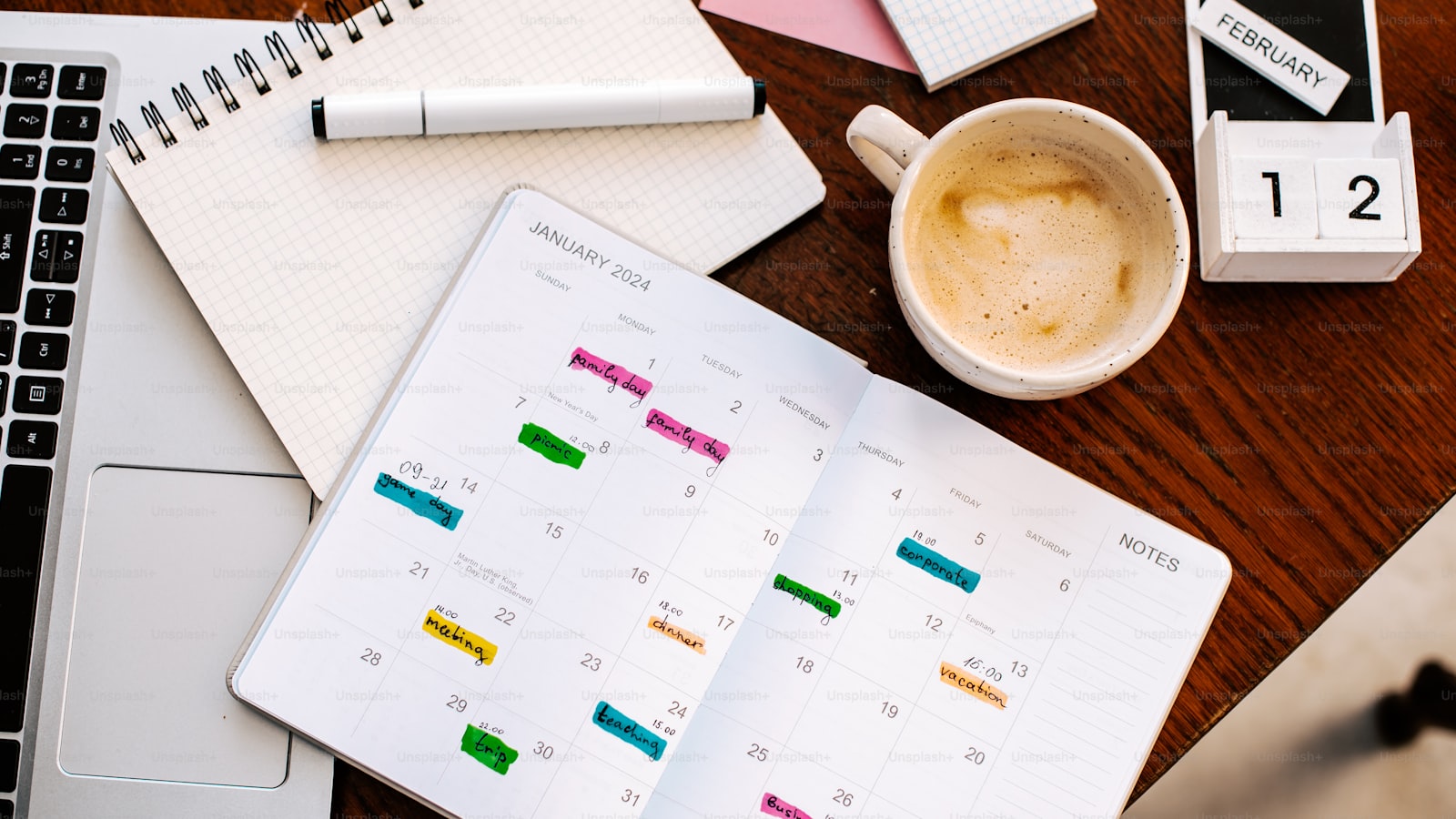 A desk with a calendar, a pen, and a laptop