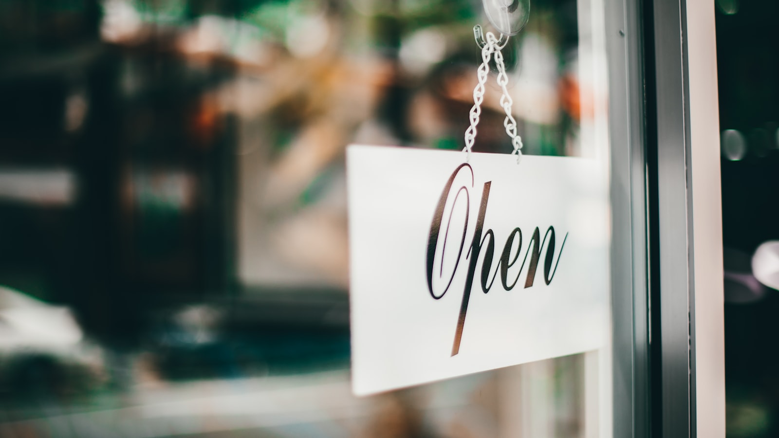 An open sign hanging on a glass shop door